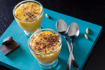 Mango lassi is a popular Indian refreshing healthy drink made of mango, yogurt and cardamom, decorated with chocolate. On a turquoise wooden background