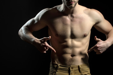 Man is pointing his fingers at his groin in jeans. Figure of athlete, naked male torso. The power...