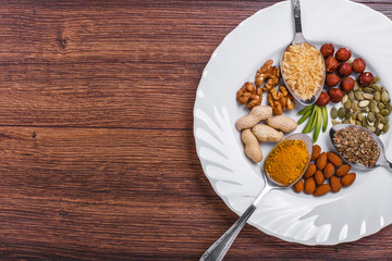 Assorted nuts in white bowl, plate on wooden surface.  peanuts, almonds, hazelnuts, pumpkin seeds, walnuts, rice , buckwheat. Top view with copy space