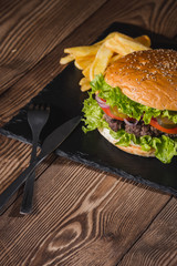 Fresh burger in bun with sesame with lettuce, tomato, beef and onion on wooden table.
