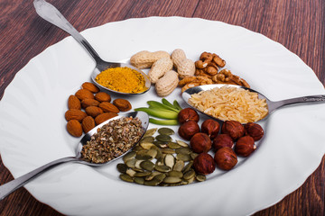 Assorted nuts in white bowl, plate on wooden surface.  peanuts, almonds, hazelnuts, pumpkin seeds, walnuts, rice , buckwheat. Top view with copy space