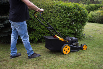 A gardener mows grass with a gasoline mower