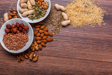 Assorted nuts in white bowl, plate on wooden surface. Top view with copy space