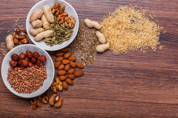 Assorted nuts in white bowl, plate on wooden surface. Top view with copy space