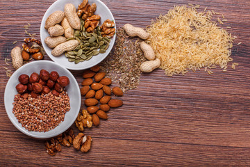 Assorted nuts in white bowl, plate on wooden surface. Top view with copy space