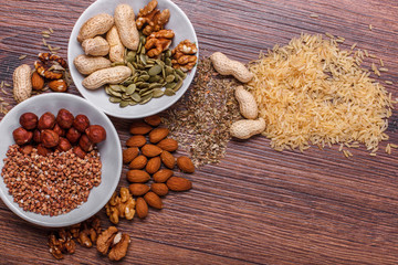 Assorted nuts in white bowl, plate on wooden surface. Top view with copy space