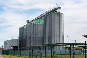 Obraz premium Grain elevator in agricultural zone and solar power station. Granary with mechanical equipment for receiving, cleaning, drying, grain shipment.