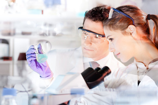 Chemical laboratory. Attractive young PhD student and her post doctoral supervisor scientist observing the blue indicator color shift after the solution  destillation.