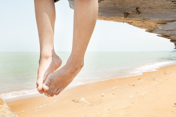 View of hanging legs on a tree bark with beach background.