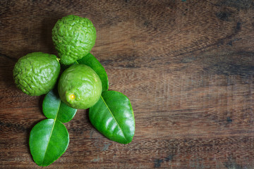 Kaffir lime and green leaves on brown wooden texture and space for contents.