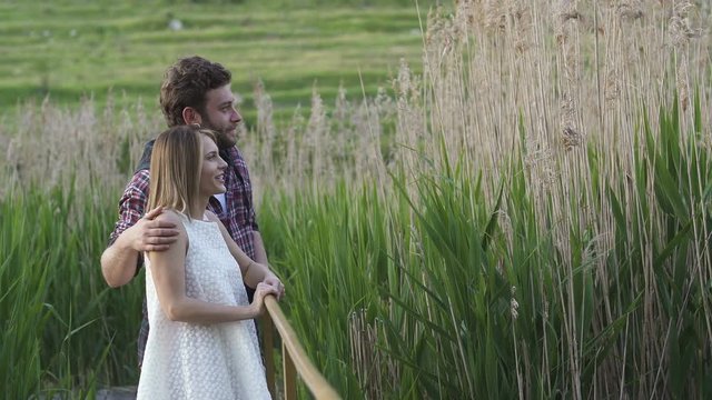Cute love couple enjoying the nature in summer time. The boy pointing something in the green bulrush to his girlfriend.