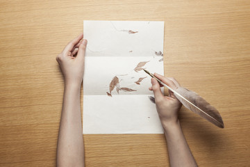 woman hand hold a feather fountain pen with letter on the wood table.