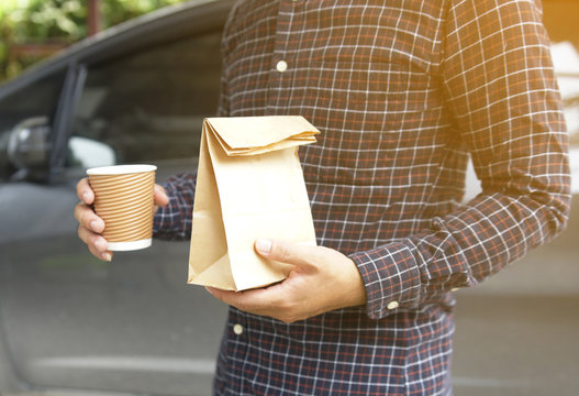 Man holding cup coffee and bread in paper bag.
