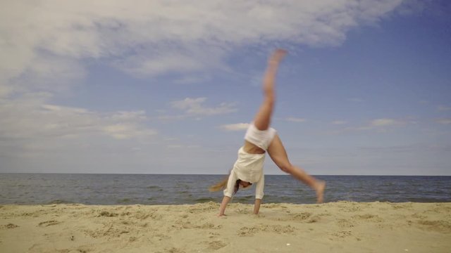 Happy girl having fun on beach. Young crazy woman playing on sea shore, dancing, doing cartwheel. Vacation happiness and craziness concept 4K ProRes HQ codec