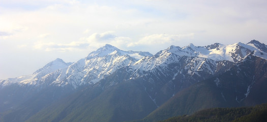 Fototapeta na wymiar Mountain landscape background. Mountain ridge with snowy peaks in fog, cloudy sky.