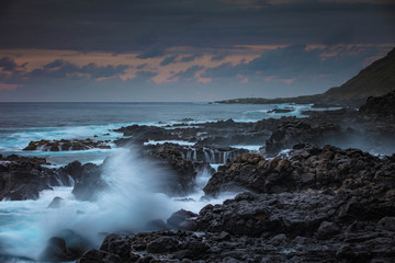 Rocky coastline with splashes of breaking waves at sunset time