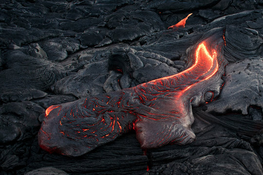Black lava field with hot red orange Lavaflow at sunset background