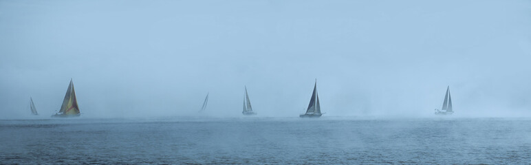 Obraz premium Sailing yachts floating in the foggy sea