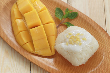 Traditional Thai dessert of mango with sticky rice mix coconut milk in wooden dish.