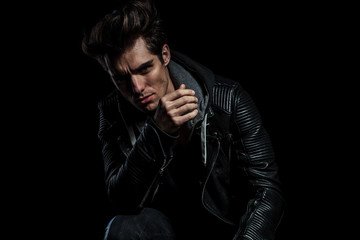 model in leather jacket resting elbow on knee while seated