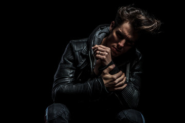 sad man in leather jacket holding his hand while sitting