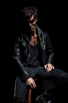 cool young man in leather jacket resting on a stool