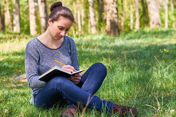 beautiful young girl in nature, making notes in a notebook