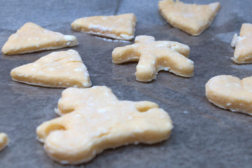 Cookie dough in different shapes lies on the baking sheet.