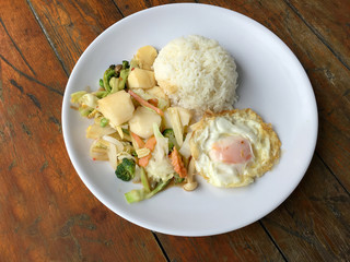 Stir-fried mixed vegetables with tofu and fried egg with rice in white dish on wooden background.  Vegetarian Food, healthy food.