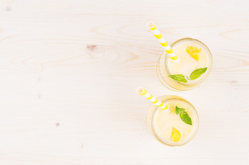 Freshly blended yellow mango fruit smoothie in glass jars with straw, mint leaves, top view. White wooden board background, copy space.