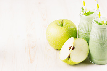 Green apple fruit smoothie in glass jars with straw, mint leaves, apples. White wooden board background, copy space.