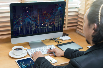 Rear view of a businessman working with a computer and tablet of business trading graphat screen on the office desk
