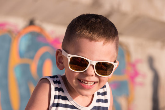 laughing little boy wearing sunglasses and sailor vest on graffiti background