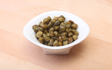 bowl with fresh capers on wooden table