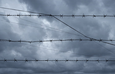 Silhouette of barbed wire over dark storm clouds before rain