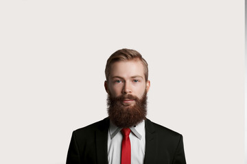 Handsome bearded top manager in black suit and red tie. Quiet emotion on man face. Guy keep tranquility and look to the camera. Big boss have speech for customers about big sale.