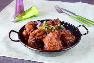 Chicken with prunes cooked in the oven in a black bowl on a textile background