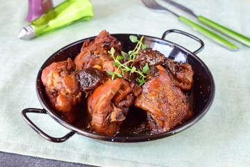 Chicken with prunes cooked in the oven in a black bowl on a textile background.