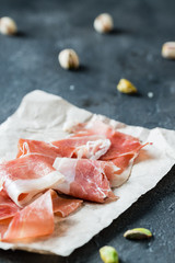 Spanish ham jamon serrano or Italian prosciutto crudo with pistachios on dark rustic background