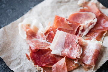 Closeup of Spanish ham jamon serrano or Italian prosciutto crudo on dark rustic background
