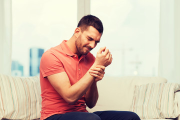 unhappy man suffering from pain in hand at home