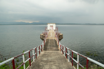 Obraz premium Wide-angle view of a concrete pier with white and red metal railings in the center, with a shed at the end. Bang Phra Reservoir, Chon Buri, Thailand.