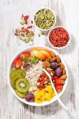 oatmeal porridge with fresh fruits and superfoods on a white wooden background, vertical, top view
