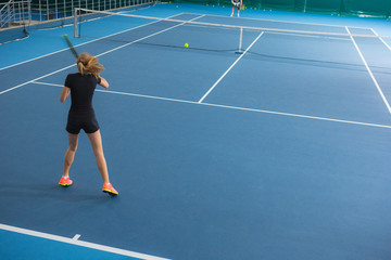 The young girl in a closed tennis court with ball