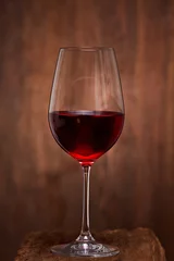 Fotobehang Close-up of crystal half-ful wineglass with red wine standing on wooden stand against wooden background. © Aleksey