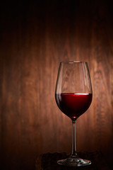 Half-full fragile wineglass of red wine standing on a wooden background.