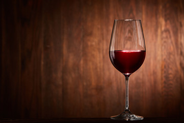 Fragile goblet of the red wine on the wooden stand on wooden wall background.