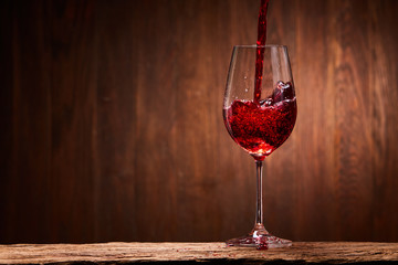 Tasty red wine poured in the elegant glass standing on the wooden stand against wooden wall background.