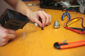 Young man hands using a black solder and soldering some wires from computer (color toned image)
