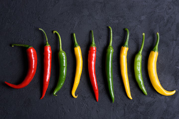 Assorted different colored chili peppers on dark background